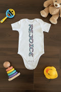 White baby romper with colorful text on a beige fabric background