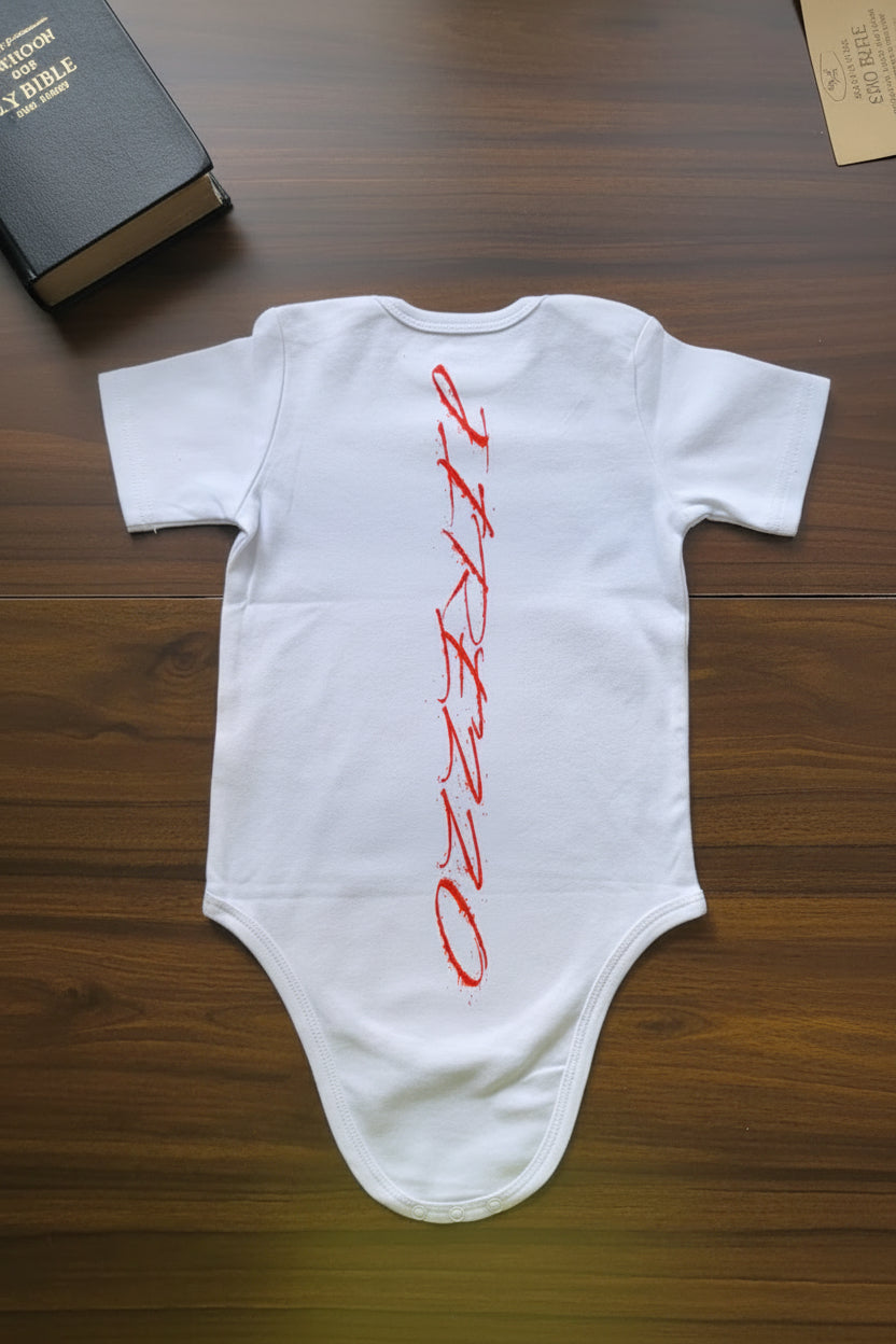 White baby onesie with red text on a wooden surface